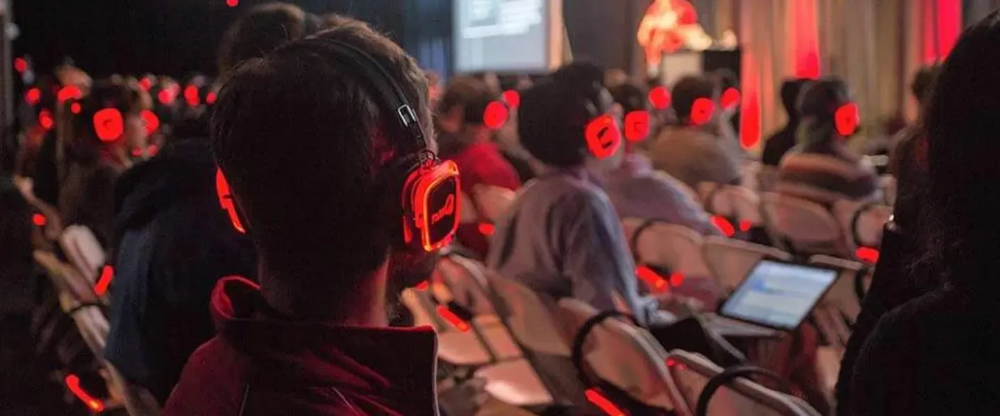 Público de una ponencia con auriculares inalámbricos iluminados en rojo