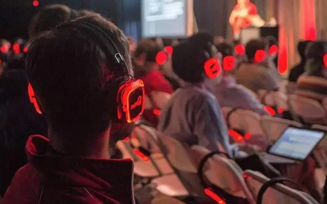 Público de una ponencia con auriculares inalámbricos iluminados en rojo
